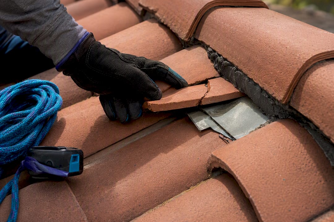 Cracked roof tile beside lifted flashing